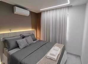 Ein modernes Schlafzimmer mit einem Bett, Nachttischen, einer Klimaanlage und einem großen Fenster mit Vorhängen.