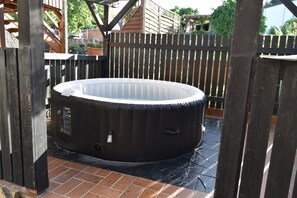 Ein Whirlpool, umgeben von einem Holzzaun, mit einer gefliesten Terrasse im Vordergrund.