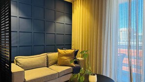 A modern living room with a dark blue accent wall, a beige sofa with cushions, a black coffee table, and a potted plant. - Cape Town Studio 16 on Bree (Cape Town)