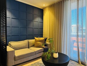 A modern living room with a dark blue accent wall, a beige sofa with cushions, a black coffee table, and a potted plant. - Cape Town Studio 16 on Bree (Cape Town)