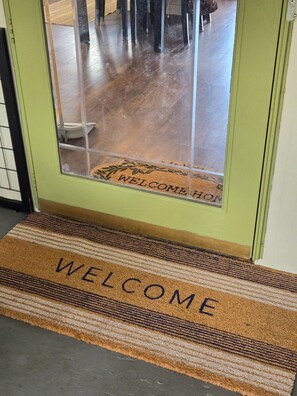 Eine Tür mit einer Fußmatte, auf der 'WELCOME HOME' steht, und einer weiteren Fußmatte mit dem Schriftzug 'WELCOME'.