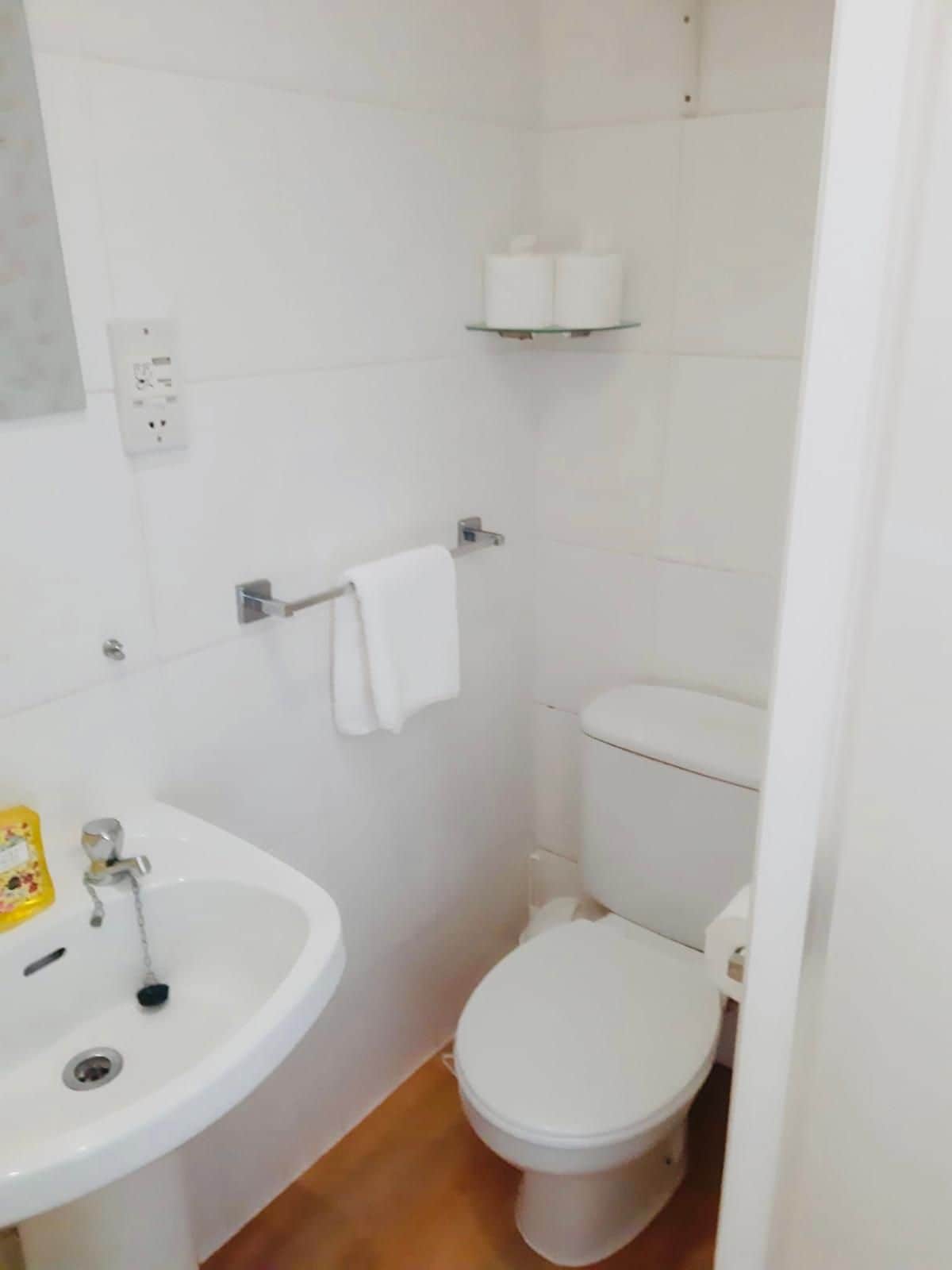 A small bathroom with a white sink, toilet, and a shelf above the toilet.