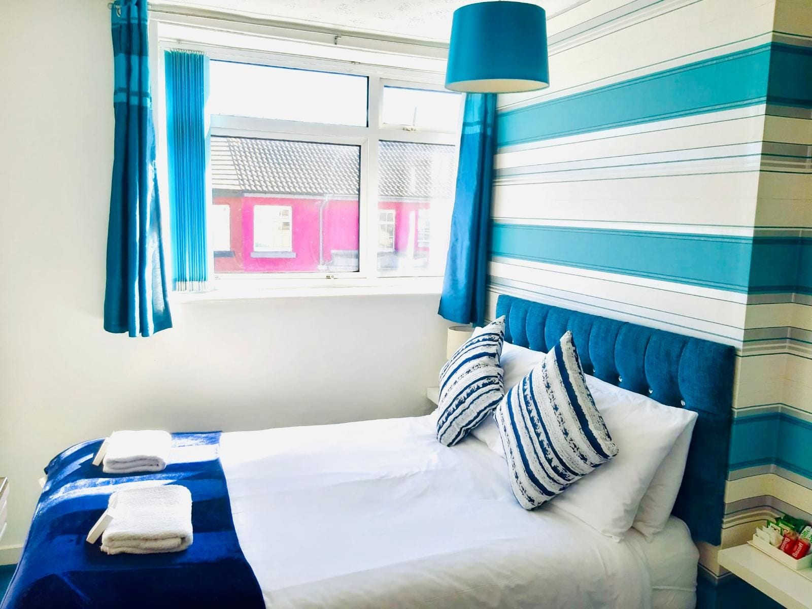 A hotel room with a bed, curtains, a window, and a striped wall.