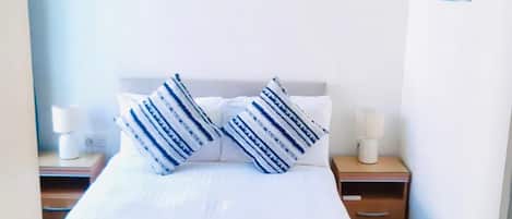 Hotellihuone, jossa on sänky, kaksi yöpöytää, yölamppu ja seinä, jossa on kaksi taideteosta.