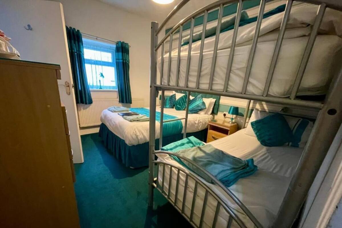 A bunk bed room with a wooden wardrobe, a window with curtains, and a bedside table with a lamp.