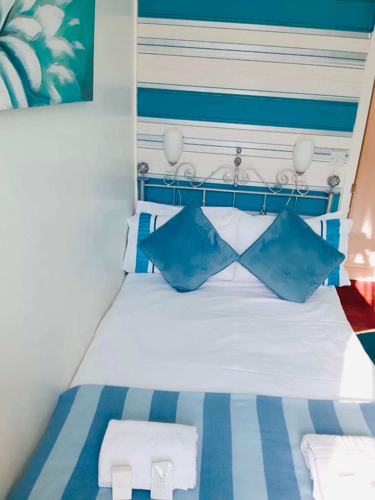 Un lit avec une couverture rayée bleue et blanche, deux oreillers, un coussin blanc et une serviette blanche posée sur le côté.