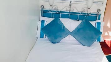 Un lit avec une couverture rayée bleue et blanche, deux oreillers, un coussin blanc et une serviette blanche posée sur le côté.