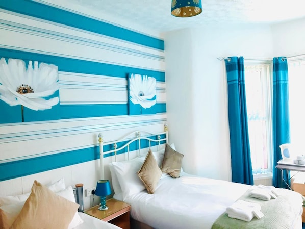 A hotel room with a bed, a nightstand, a lamp, and a window with curtains. - The Beeches Hotel (Blackpool)