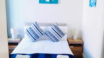 A hotel room with a bed, two bedside tables, a nightstand, and a wall with two pieces of artwork.