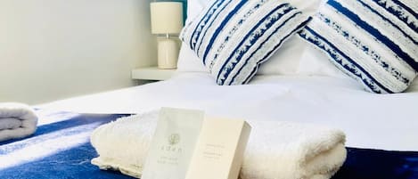 A neatly made bed with a blue blanket, white pillows, and a set of toiletries including a bottle and a box.