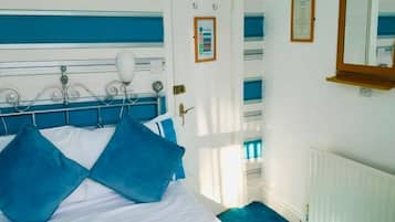 A hotel room with a bed, a bedside table, a mirror, a radiator, and a door with a sign.