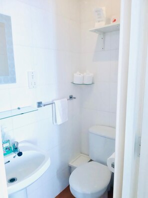 A small, white bathroom with a sink, toilet, and a glass shelf above the toilet. - The Beeches Hotel (Blackpool)