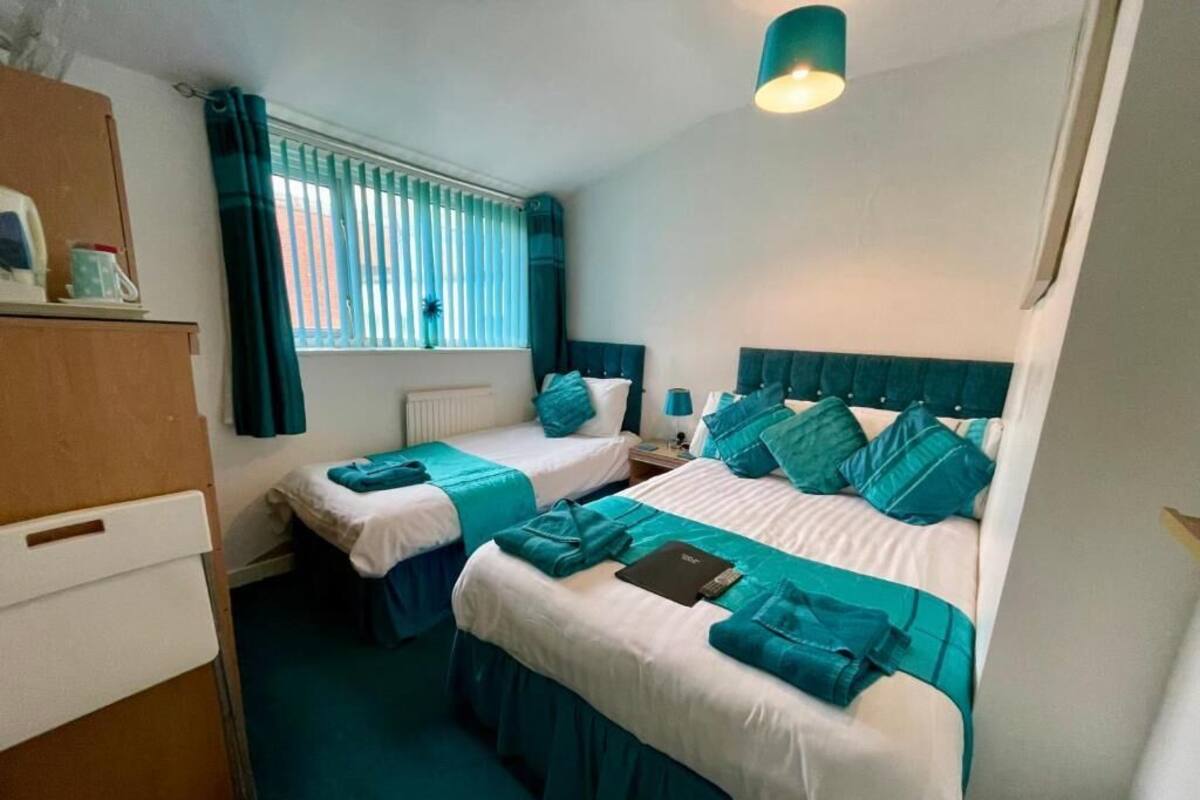 A hotel room with two beds, a dresser, a window with curtains, and a ceiling light.