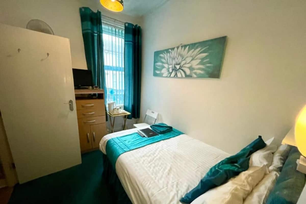 A bedroom with a bed, a desk, a chair, a wardrobe, and a painting on the wall.