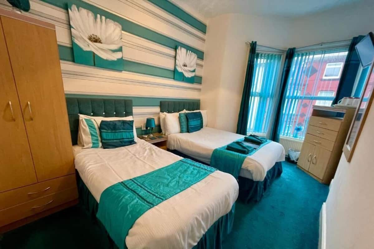 A hotel room with two beds, a wooden wardrobe, a television, and a window with curtains.