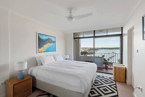 Ein Schlafzimmer mit Bett, Nachttisch, Lampe, Gemälde und einem Balkon mit Blick aufs Wasser.