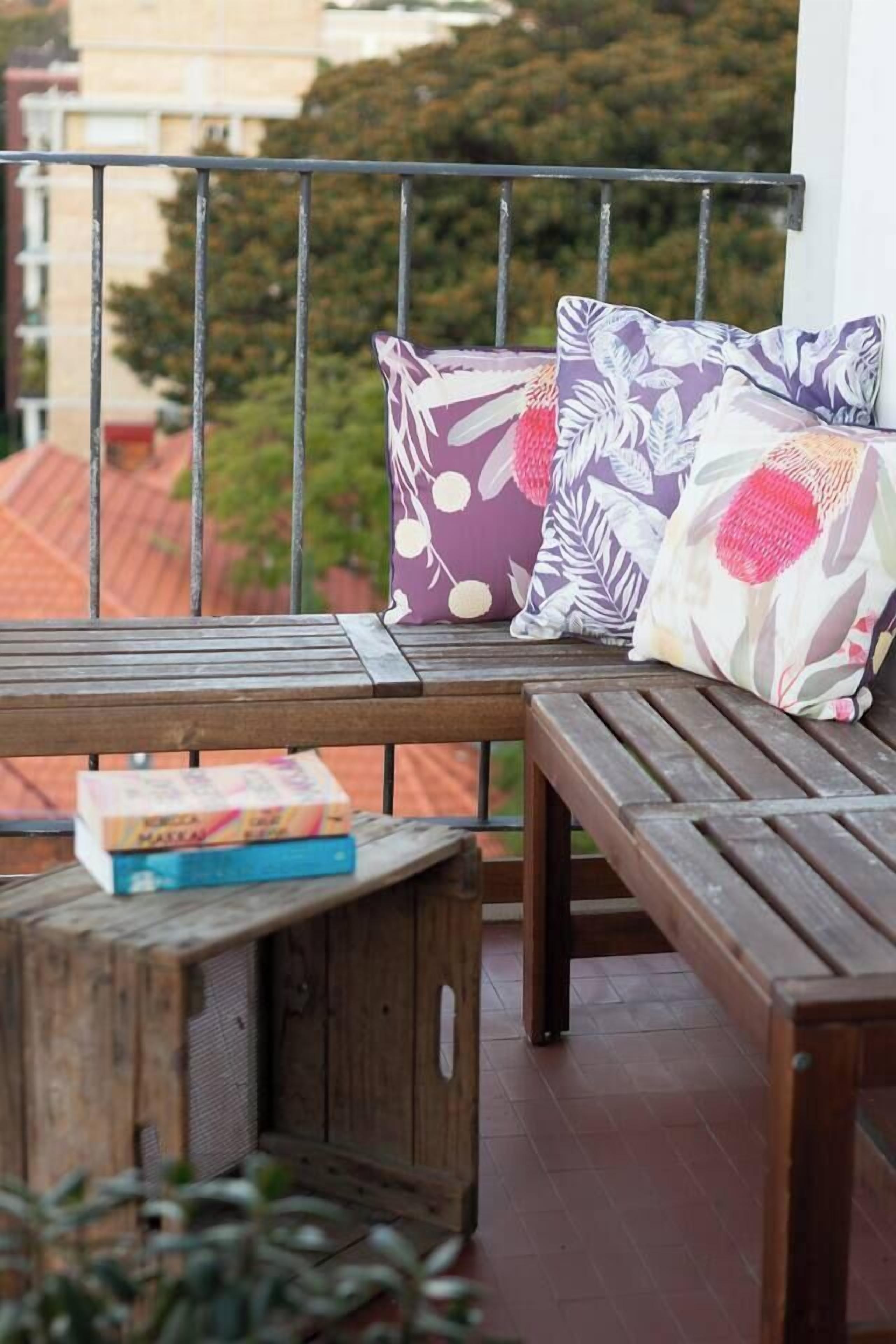 Un balcon agrémenté de meubles en bois, notamment d’un banc et d’une petite table, ainsi que de plusieurs coussins aux motifs floraux.