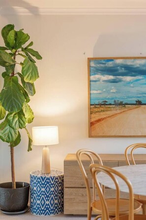 Ein Essbereich mit Tisch, Stühlen, einer Topfpflanze, einer Lampe und einem Bild an der Wand.
