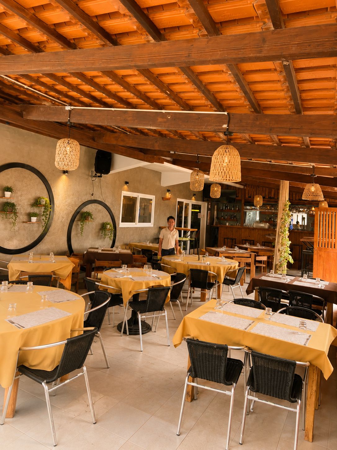 Un comedor interior con mesas redondas, sillas negras e lámparas colgantes.