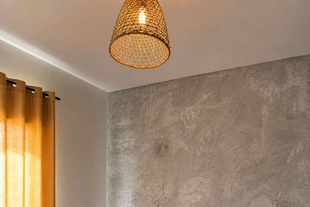 Un dormitorio moderno con una cama grande, pared gris con textura y una lámpara colgante.