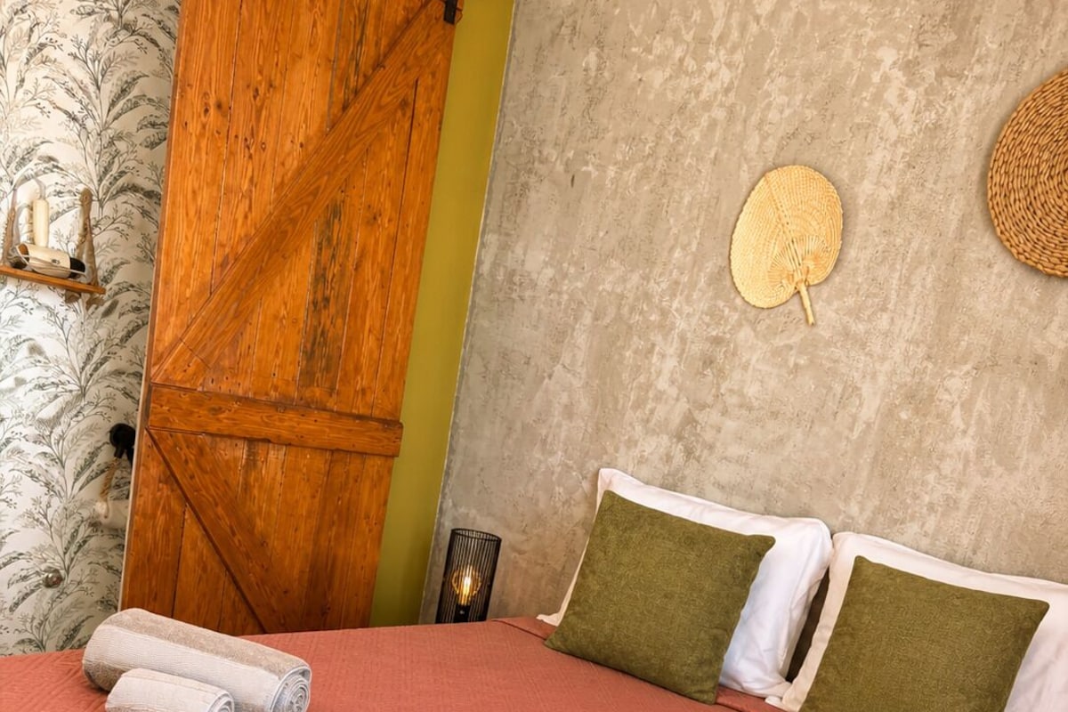 A bed with a patterned bedspread, two rolled towels, and two pillows with different textures.