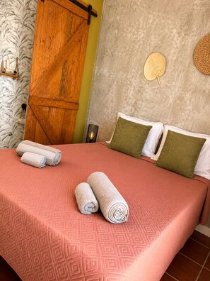 Una cama con una colcha estampada, dos toallas enrolladas y dos almohadas de diferentes texturas.