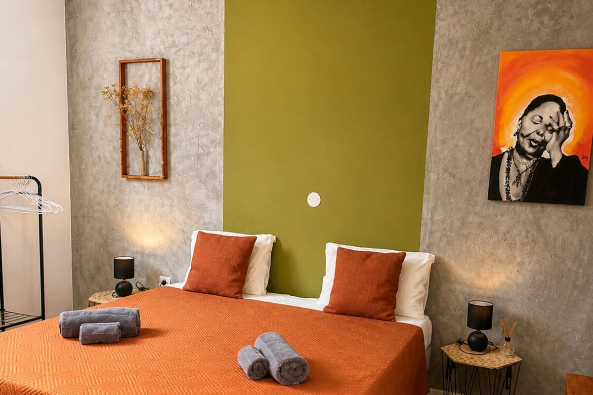 A hotel room with a large bed, two bedside tables, a wall-mounted lamp, a framed picture, and a painting.