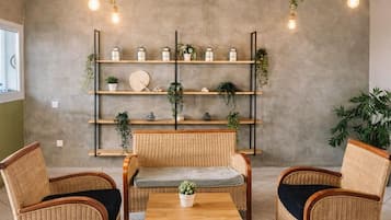 Una habitación con muebles de mimbre, una mesa central y estantes con plantas y adornos.