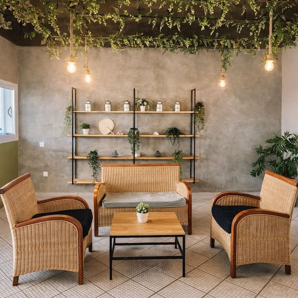 Una habitación con muebles de mimbre, una mesa central y estantes con plantas y adornos.