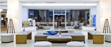 Un vestíbulo moderno con una zona de estar central, paredes de vidrio y vistas al interior.