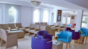 Un vestíbulo de hotel con varias zonas de estar, que incluyen sillas y sofás, y un mostrador de recepción.