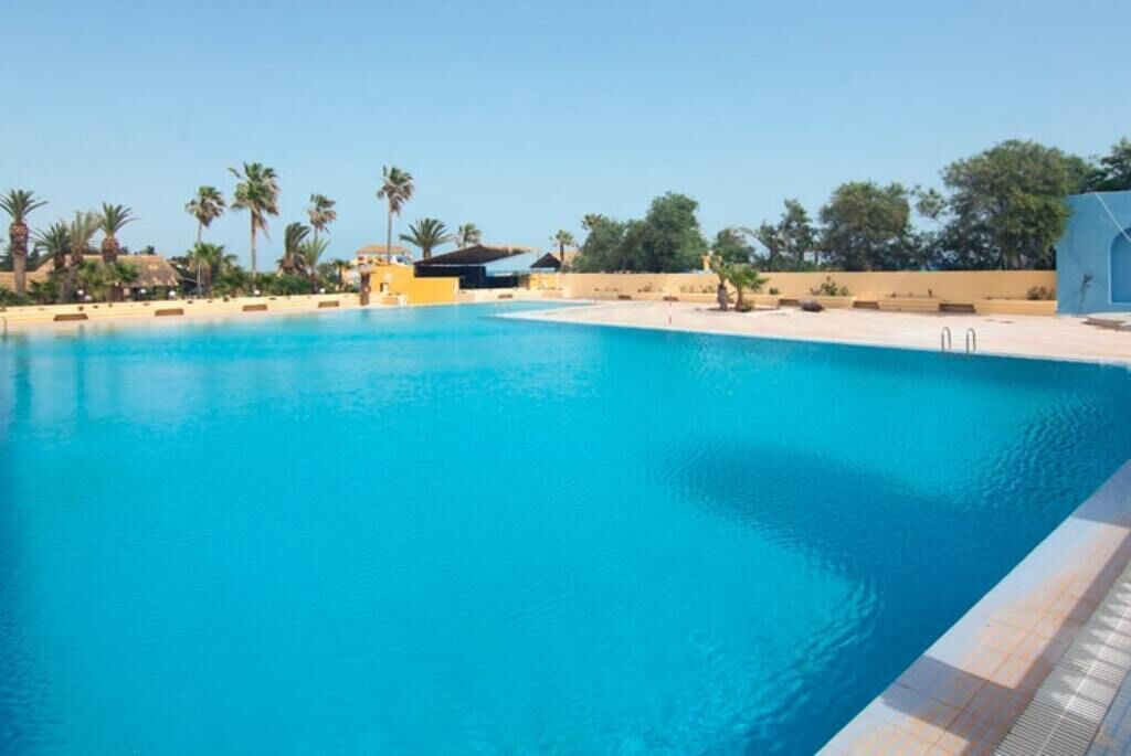 Una piscina con agua azul cristalina, rodeada de palmeras y edificios.