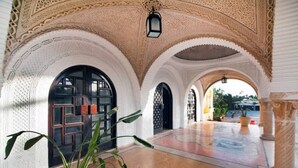Un pasillo interior con arcos, una planta en maceta y suelo de baldosas.