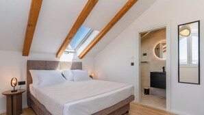 Ein Schlafzimmer mit Bett, Nachttischen, einem Oberlicht, einem Badezimmer mit Spiegel und Blick ins Freie.