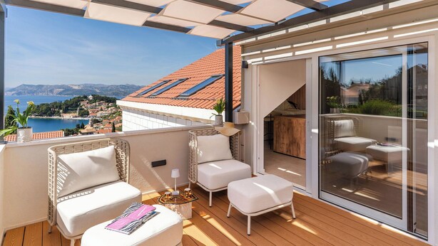 Ein Balkon mit Sitzgelegenheit im Freien, Blick auf eine Küstenstadt und eine Glastür zu einem Innenbereich.