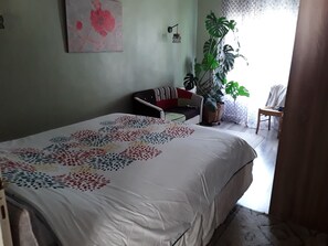 A bedroom with a bed, a chair, a sofa, a potted plant, and a wall-mounted light fixture. - HAMLET HOUSE in the heart of the mountains (Breil-sur-Roya)