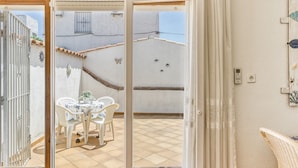 A room with a tiled floor, a white table with chairs, a small potted plant, and a view of a neighboring building through an open door. - 'Bahia Studio' Apartment with Lake Views, Wi-Fi, and Air Conditioning (Empuriabrava)