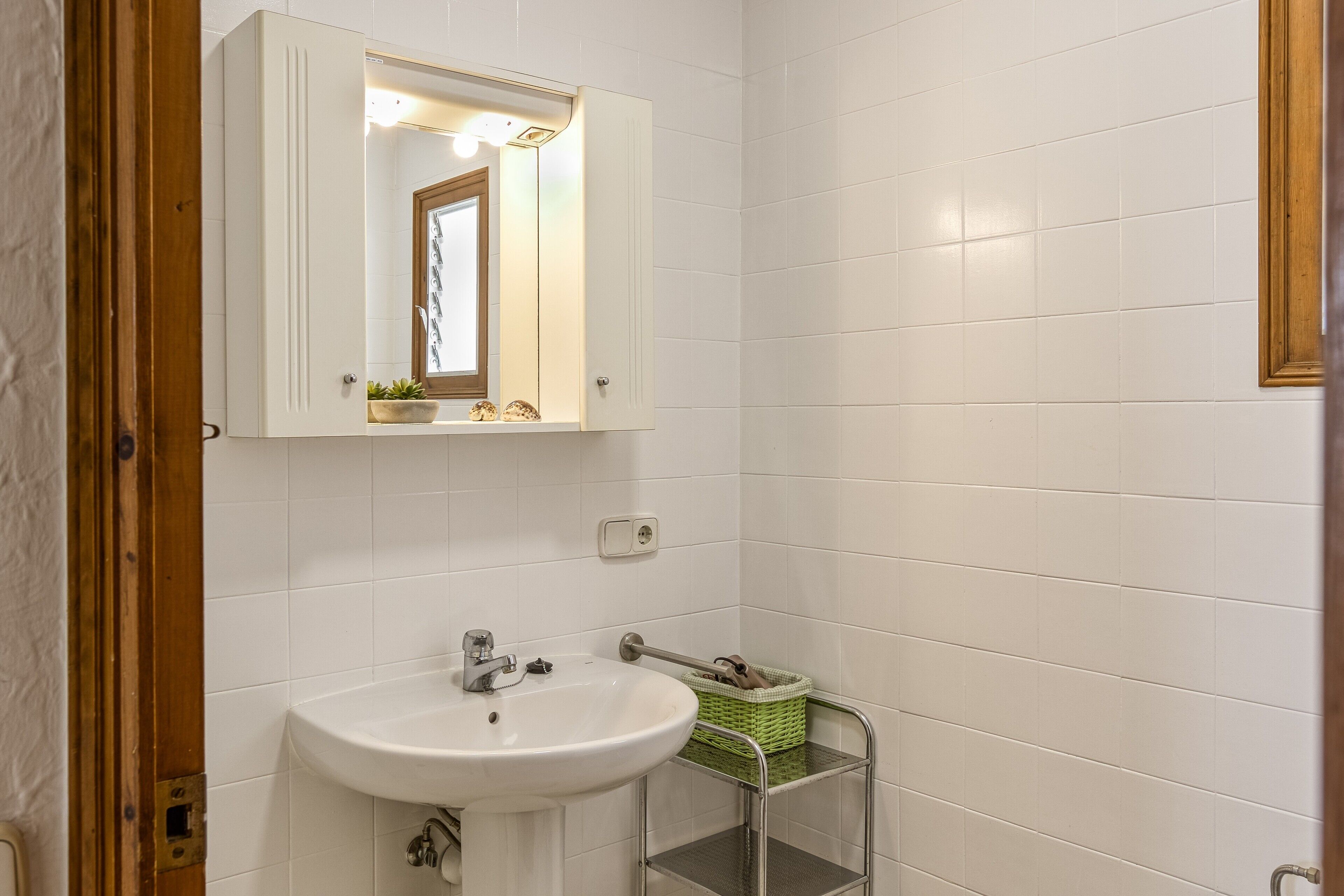A bathroom with a white sink, a mirror, and a green basket on a metal shelf.