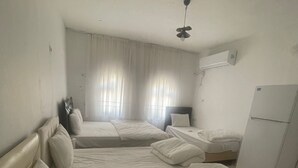 Una habitación con tres camas, ventilador de techo, aire acondicionado y refrigerador.