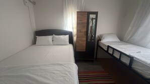 Una habitación pequeña y limpia con dos camas individuales, un armario de madera y un tapete a rayas.