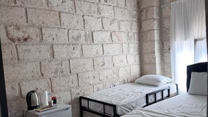 Una habitación con pared de ladrillo, una cama, un refrigerador pequeño y una ventana con cortinas.