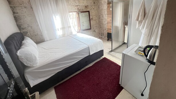 Un dormitorio con cama, un escritorio pequeño con hervidor, espejo y zona de ducha.