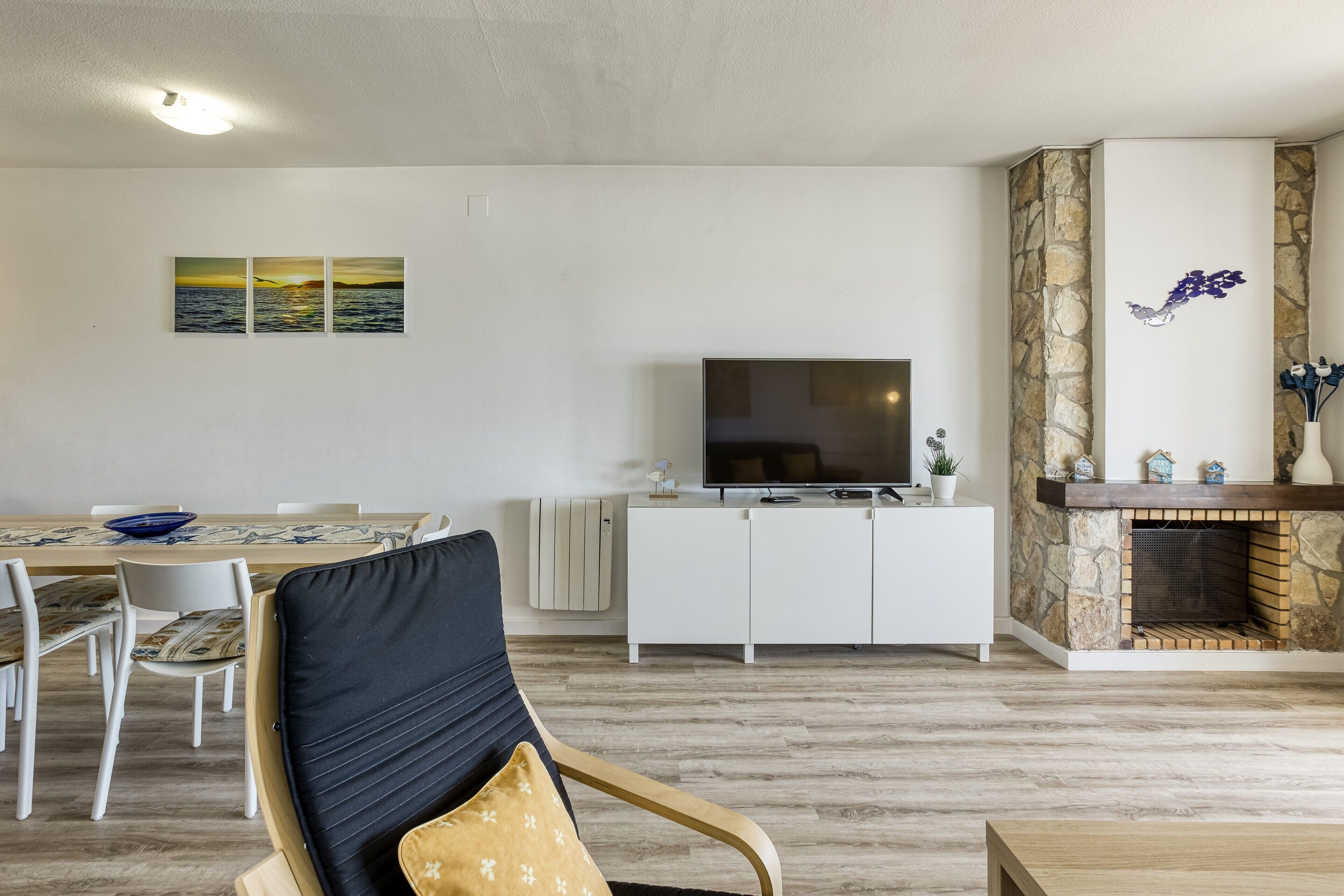 Ein Wohnzimmer mit Sofa, Fernseher, Kamin, Esstisch, Stühlen und Kunstwerken an der Wand.