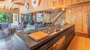 A modern kitchen with a central island, wooden walls, and a view of the outdoors. - Villa Yucca - Cap Ferret *Heated pool *Market *Beaches (Lège-Cap-Ferret)