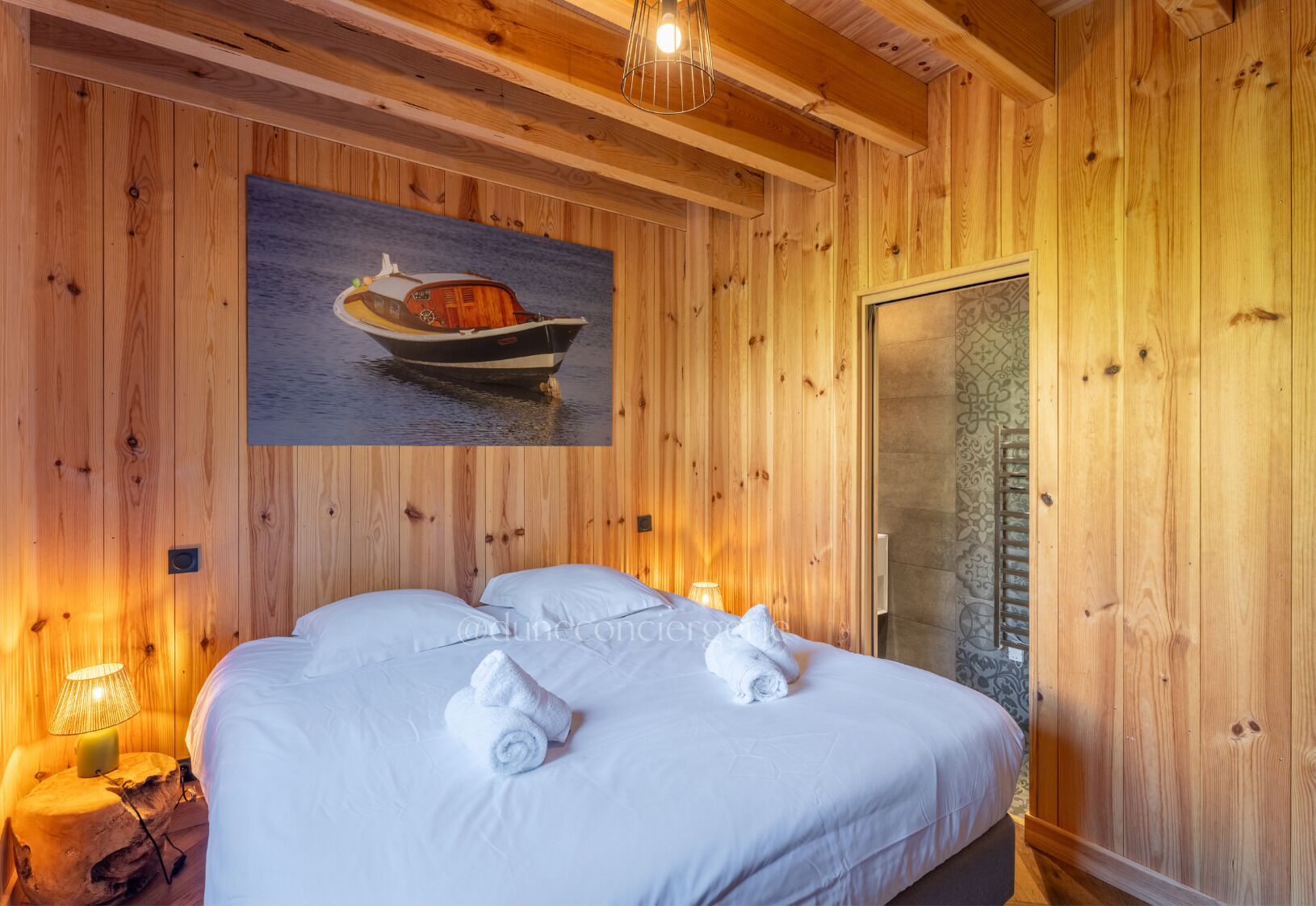 Une pièce aux murs lambrés, avec un lit, un tableau représentant un bateau et une porte.