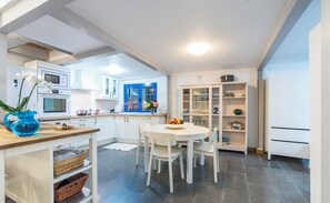 A modern kitchen with white cabinets, a blue-framed window, and a dining area with a white table and chairs.