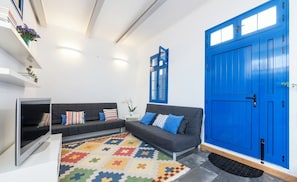 Un salon moderne avec un ensemble de canapés, un téléviseur, un tapis coloré et une porte bleue.