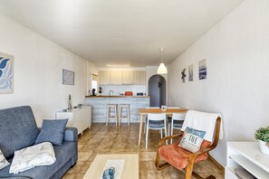 Ein kompakter Wohnbereich mit einer Couch, einem Esstisch mit Stühlen, einer Küchenzeile und einer kleinen Sitzecke mit einem Sessel.