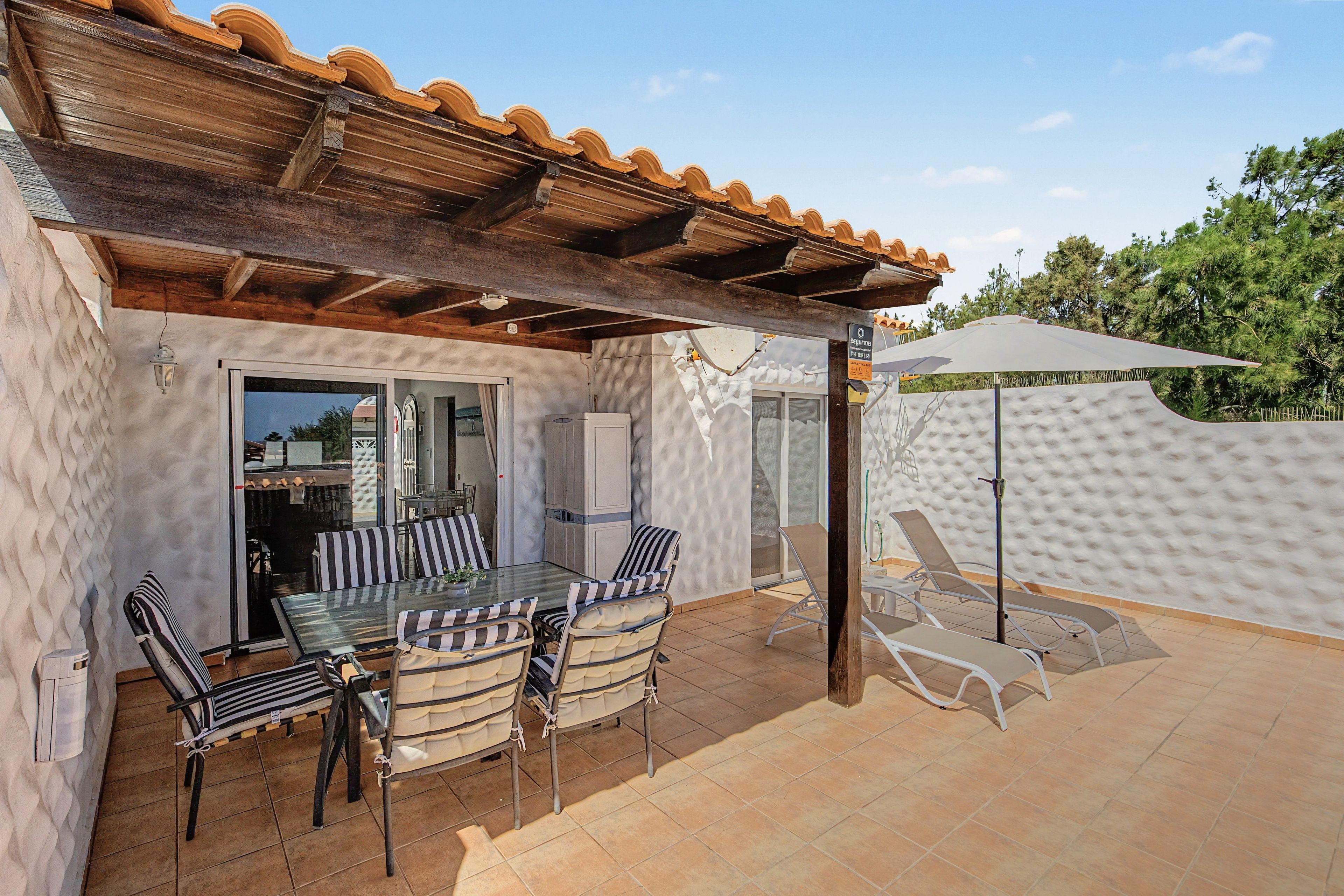 A covered outdoor patio with a table and chairs, a pergola, and a sun umbrella.