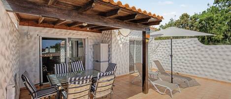 A covered outdoor patio with a table and chairs, a pergola, and a sun umbrella.